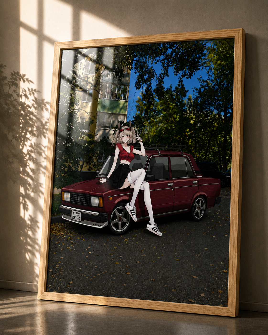 A framed art print leaning against a wall in a sunlit room. The print shows an anime-style woman sitting on a dark red vintage car outdoors, with trees, a building, and blue sky visible.
