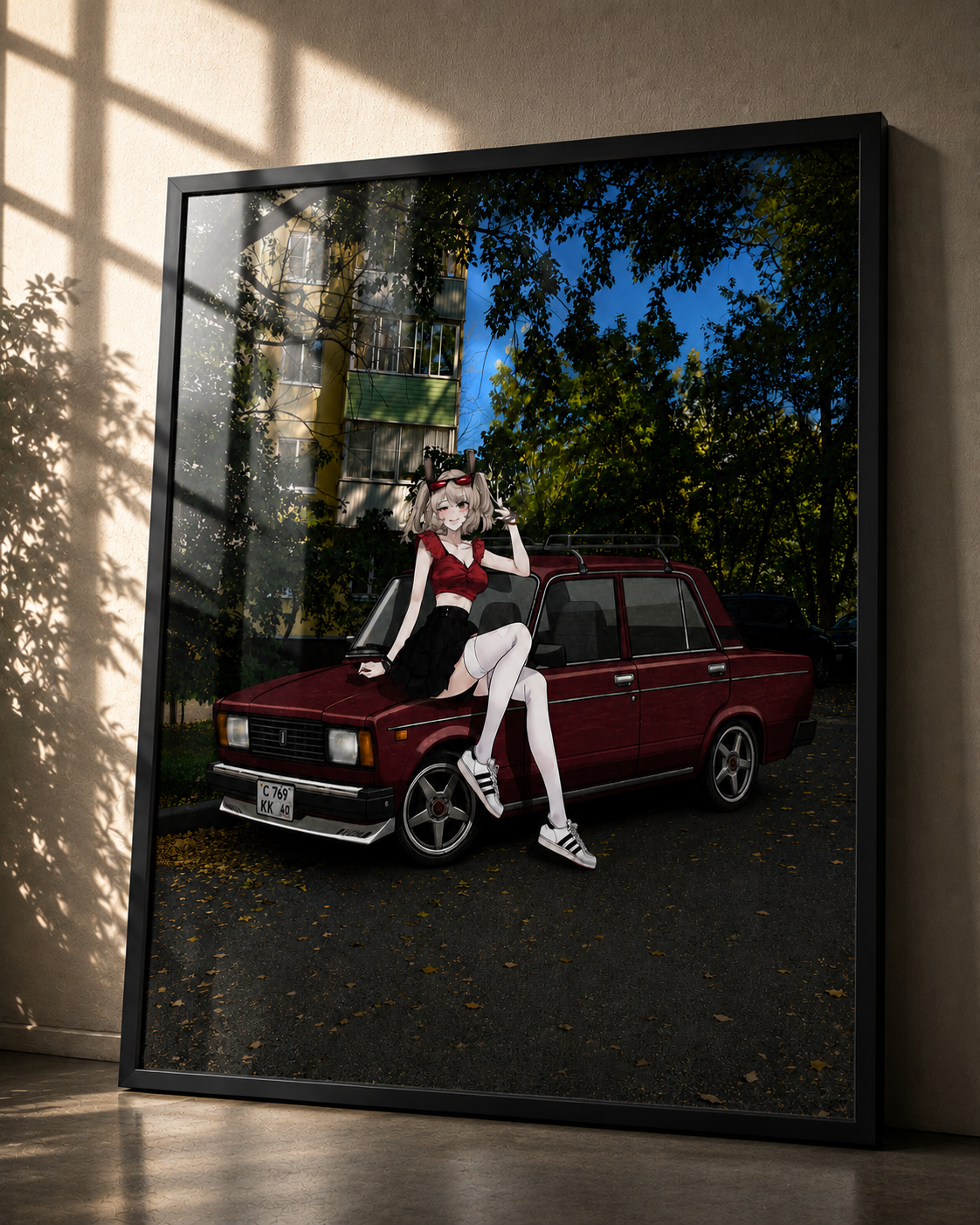 A framed art print leaning against a wall in a room. The print shows an anime-style girl with pink hair sitting on a dark red vintage car, with trees and a blue sky in the background.